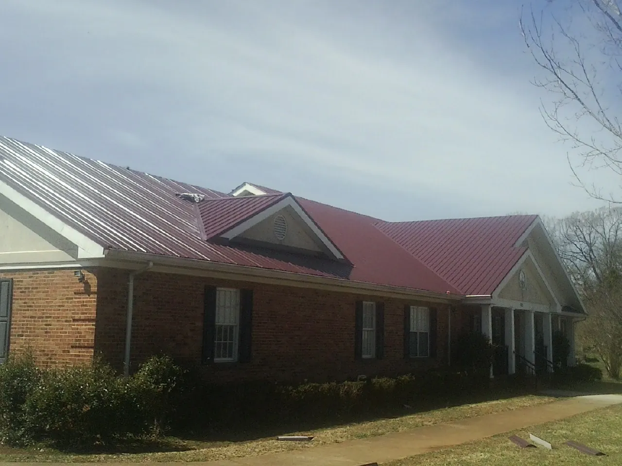 Red metal roof with gabled entries on a long brick building, from a Hail Damage Roof Repair job in Marysville